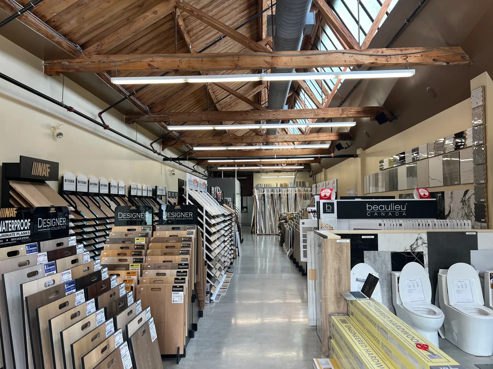 The showroom's centre aisle, lined with flooring sample boards under a timber-trussed roof with skylights.