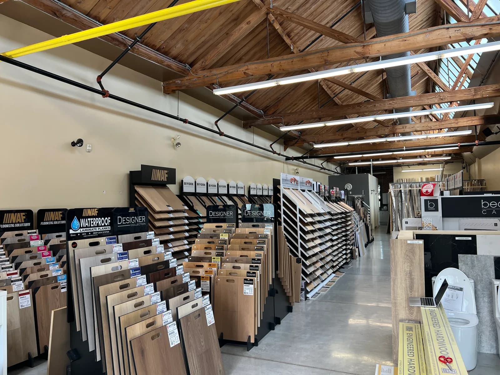 Inside the Queen Street showroom: flooring displays either side of a wide aisle, under a timber-trussed roof lit by skylights.
